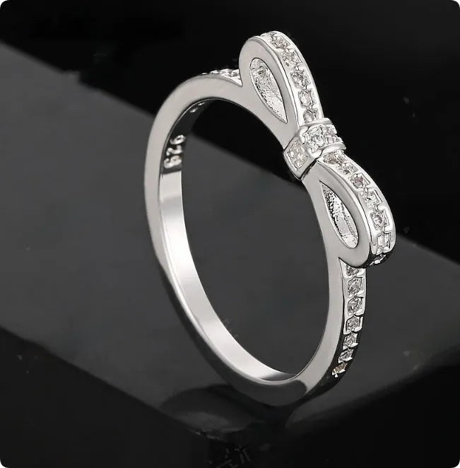 Silver couple ring with bow shape and rhinestone zircon crystals on finger.