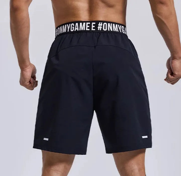 Man wearing loose black sports shorts with letter print detail, showing elastic waist and cropped length.