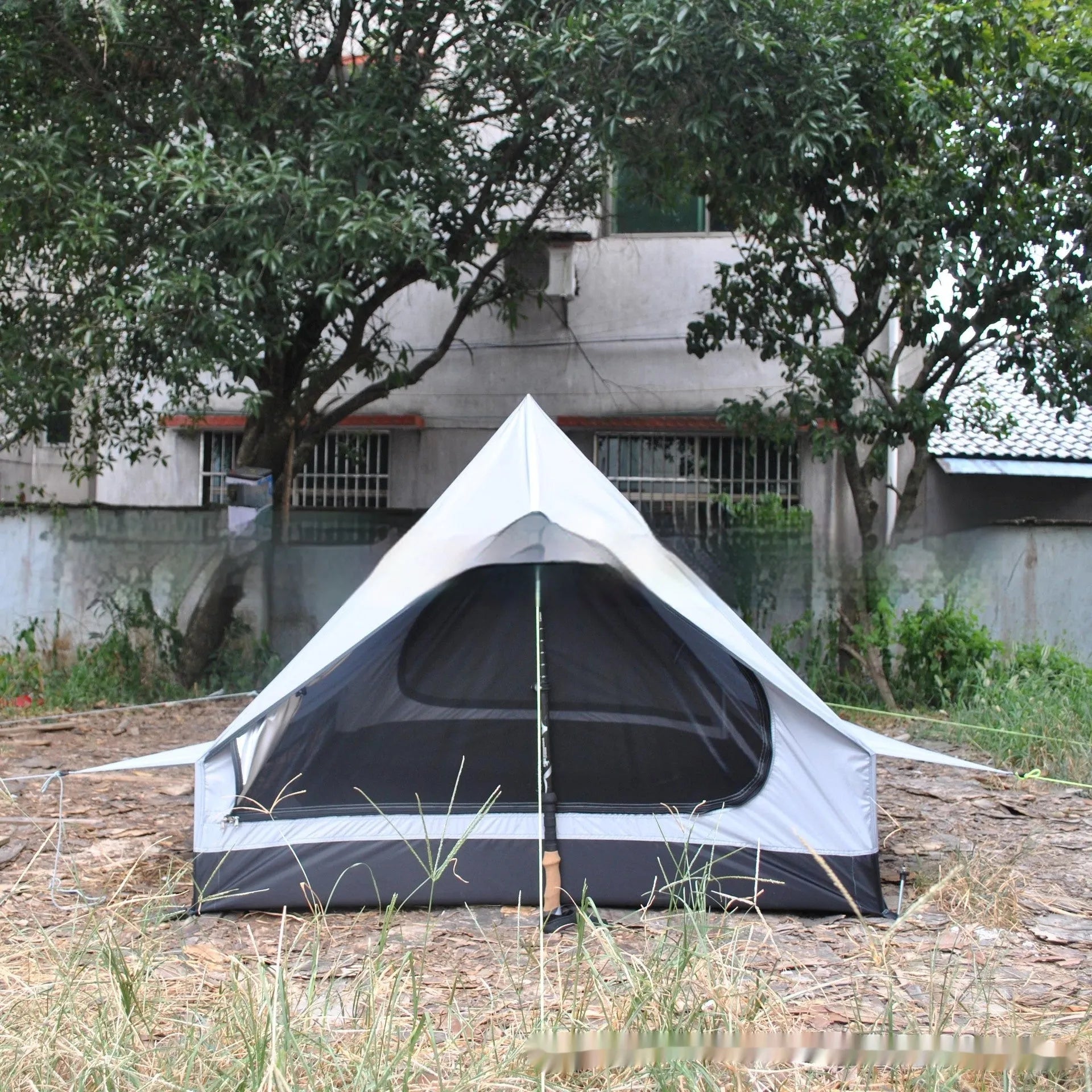 Brown A-line cabin tent pitched using hiking poles with aluminium ground nails and fluorescent wind ropes