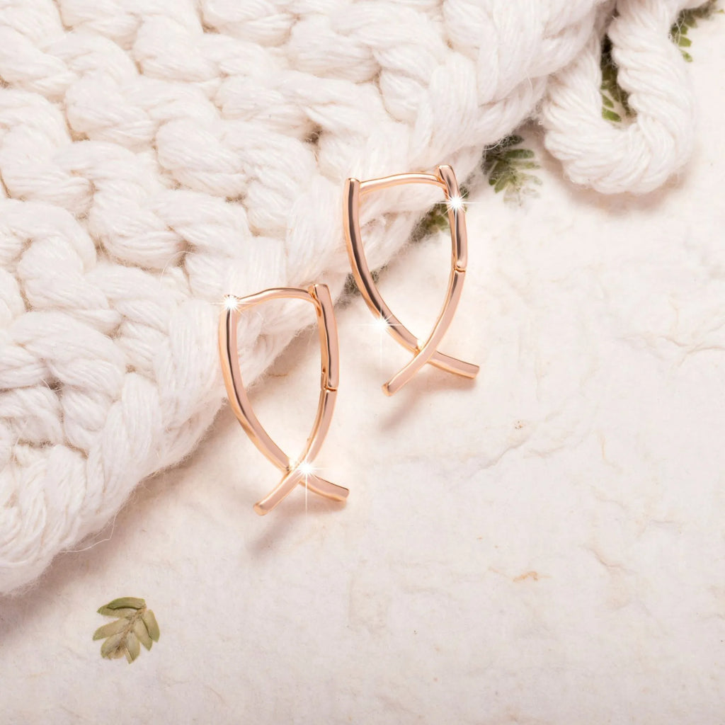 Rose gold coloured cross-shaped drop earrings for women on a white background.