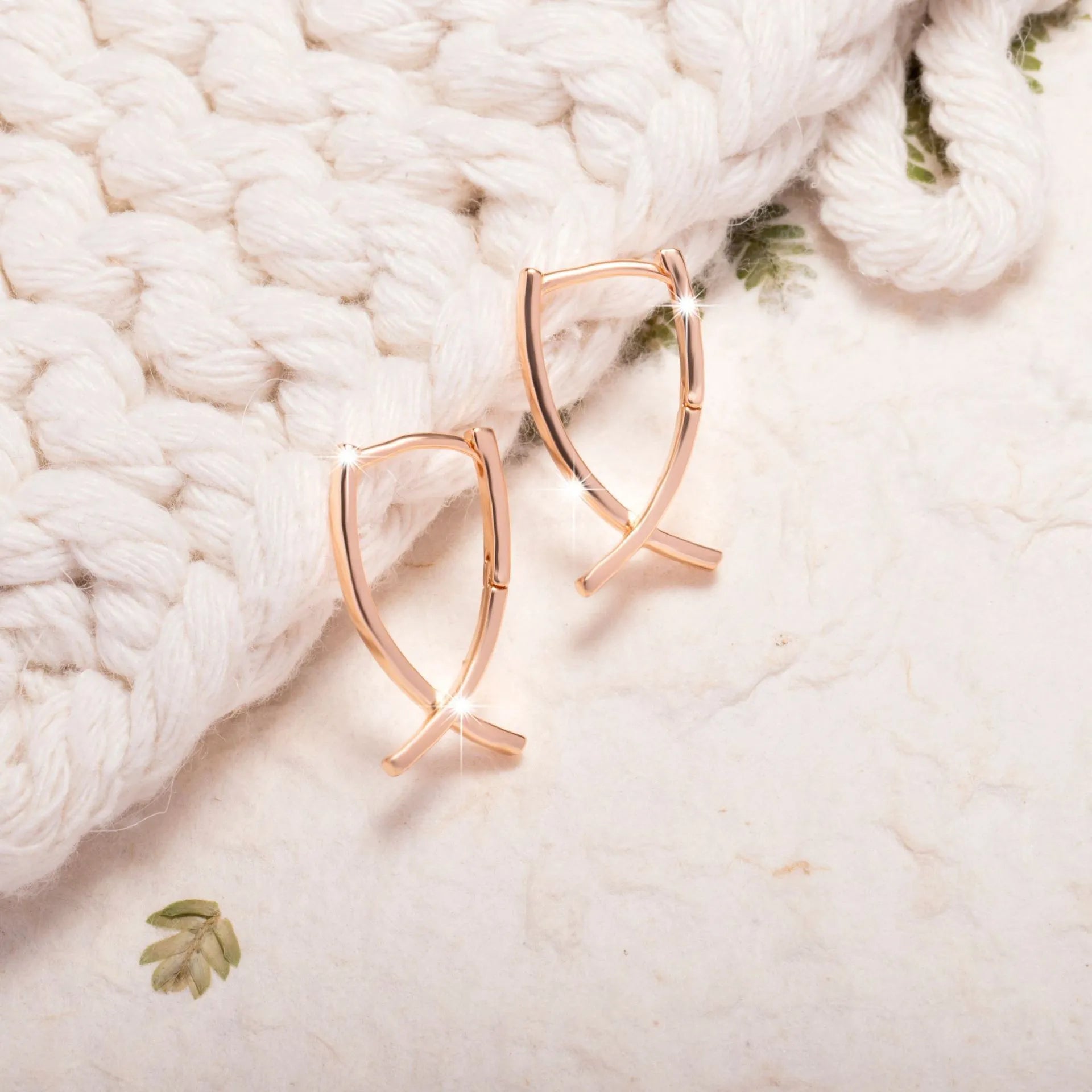 Rose gold coloured cross-shaped drop earrings for women on a white background.
