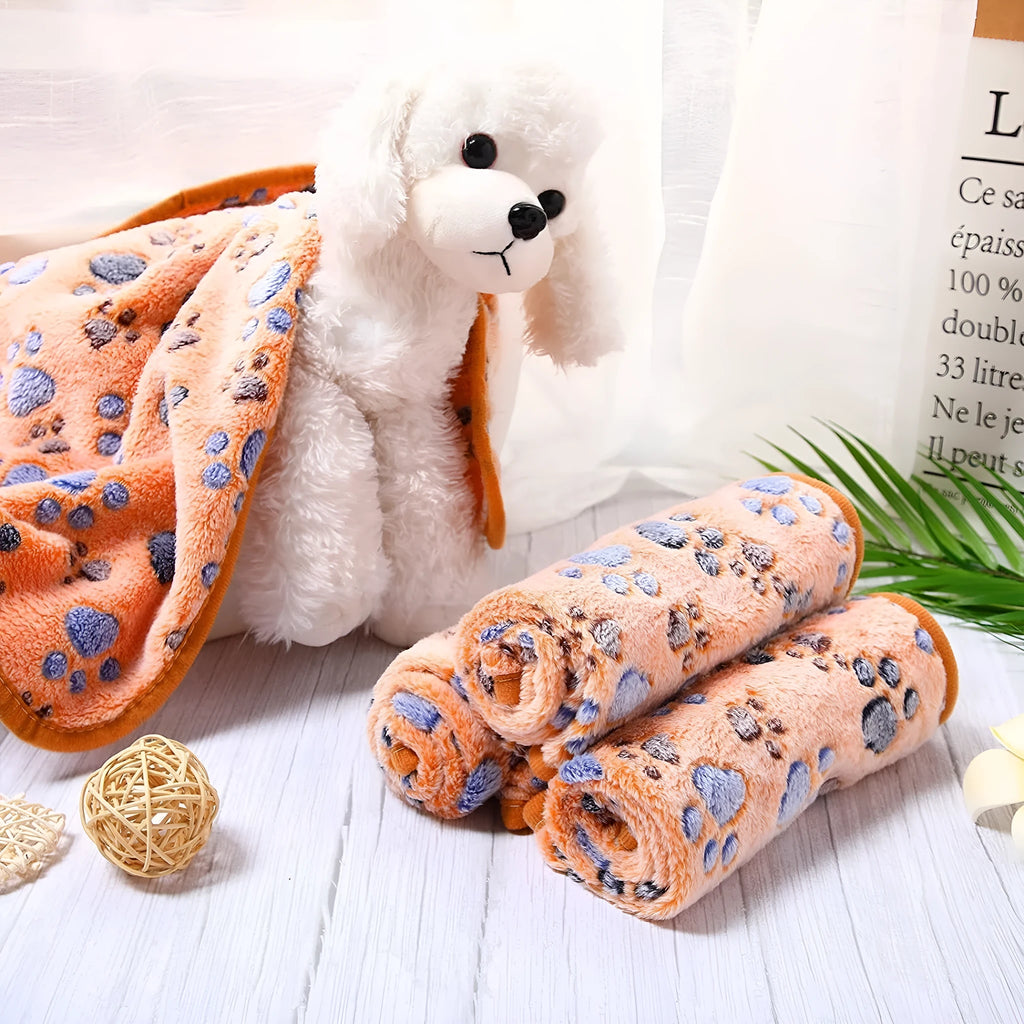 Coral fleece dog blanket with paw print pattern in beige, shown on a dog bed.