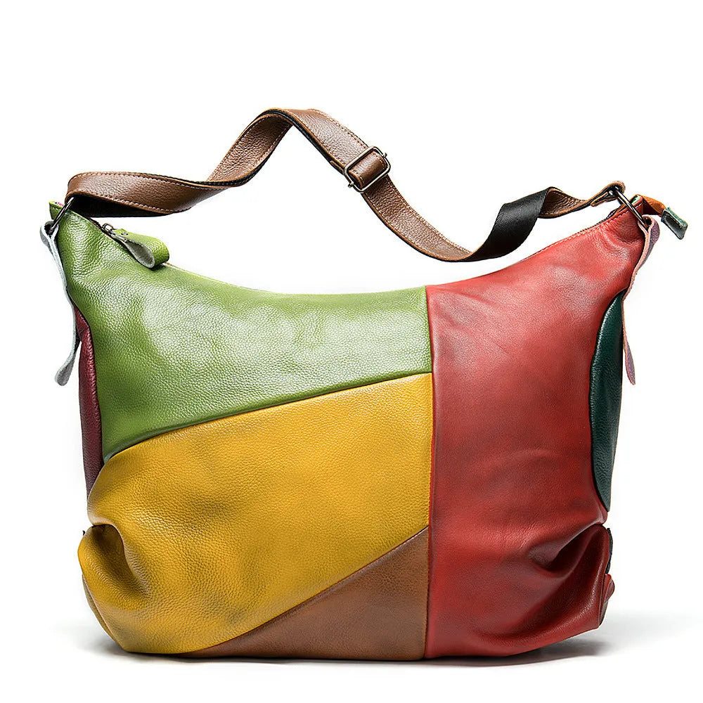 Brown cowhide leather crossbody travel bag with stitching details, shown next to a laptop and magazine.