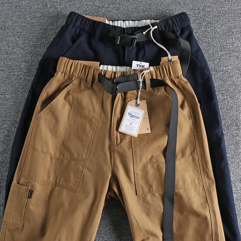 Man wearing mid-waist khaki cotton work trousers with a zipper fly and straight leg cut.