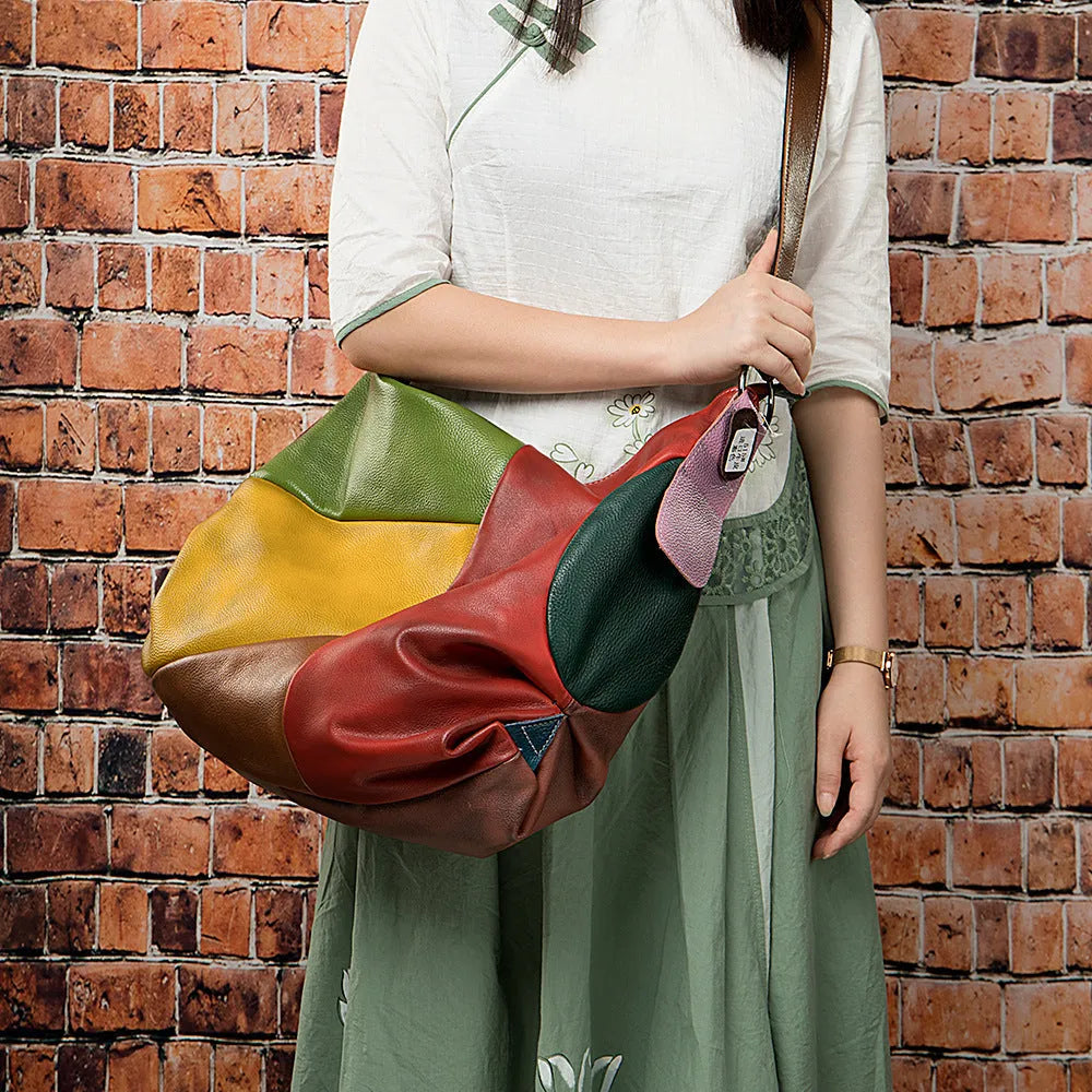 Brown cowhide leather crossbody travel bag with stitching details, shown next to a laptop and magazine.