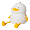 Chubby white silicone night lamp on a desk holding a mobile phone, showing soft LED glow.
