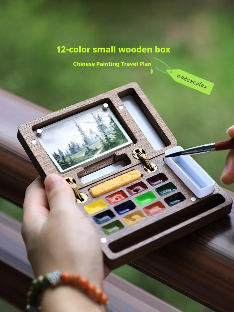 Mini walnut wood watercolour paint box open to show paint pans, with Holbein and Schminke pigment suit options.