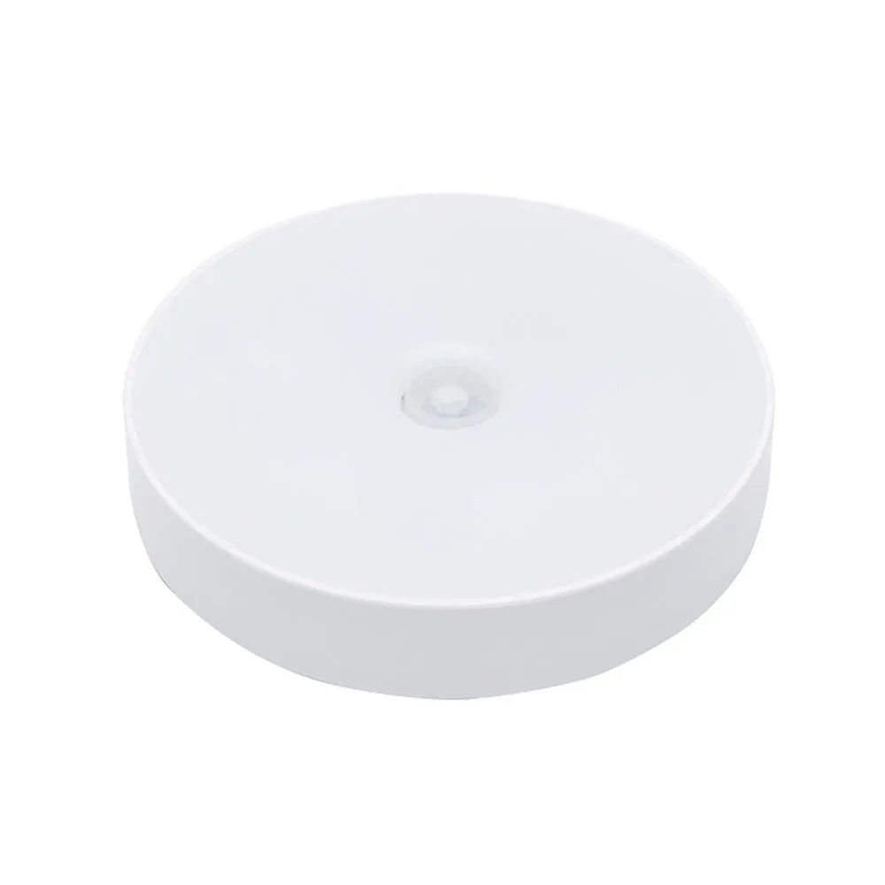 Small circular white motion sensing LED night light with USB charging cable and adhesive tape.