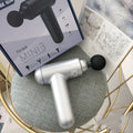 Black fascia gun massager with USB charging port shown alongside red and white colour variants