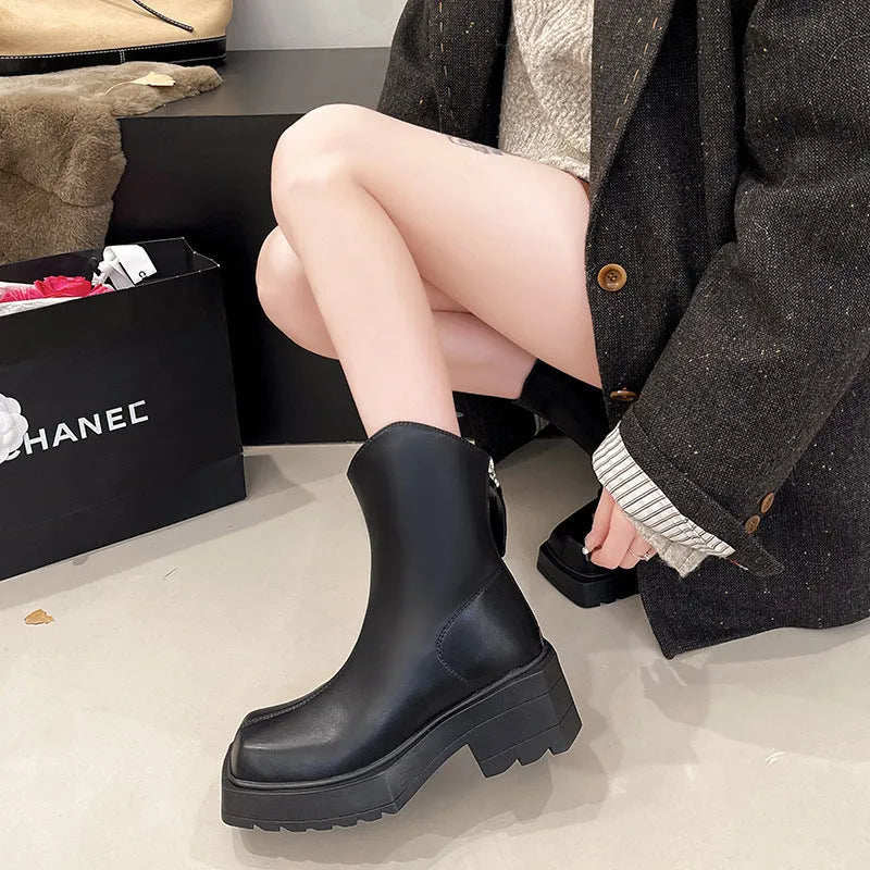 Black platform Martin ankle boots with a square toe, chunky heel, and back zipper on a woman's feet.
