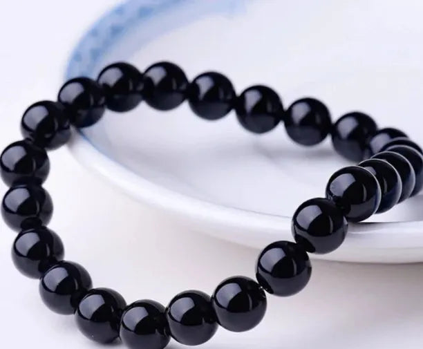 Close-up of a women's black onyx agate bracelet with 8mm geometric beads on a black elastic cord.
