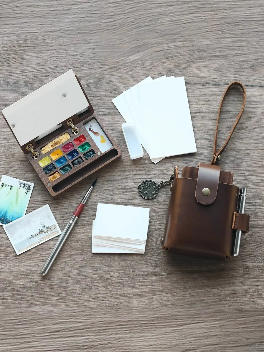 Mini walnut wood watercolour paint box open to show paint pans, with Holbein and Schminke pigment suit options.