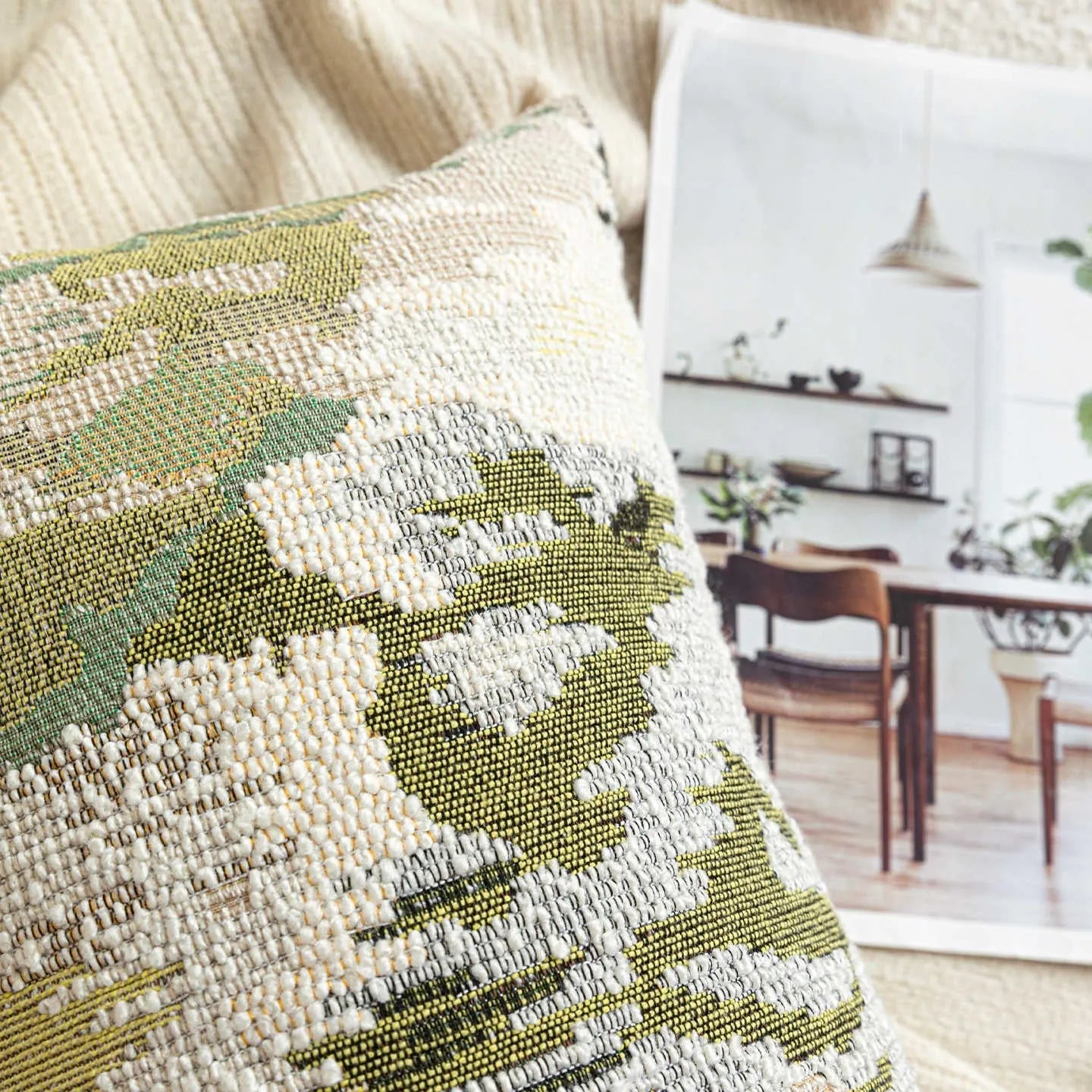 Antique green square pillow with abstract spring flowers pattern on a grey sofa.