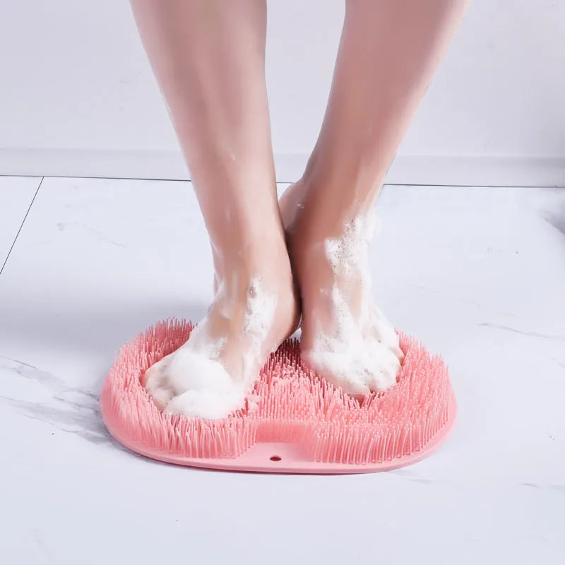 Orange non-slip massage bath brush with suction cups and soft silicone bristles on a bathroom floor.