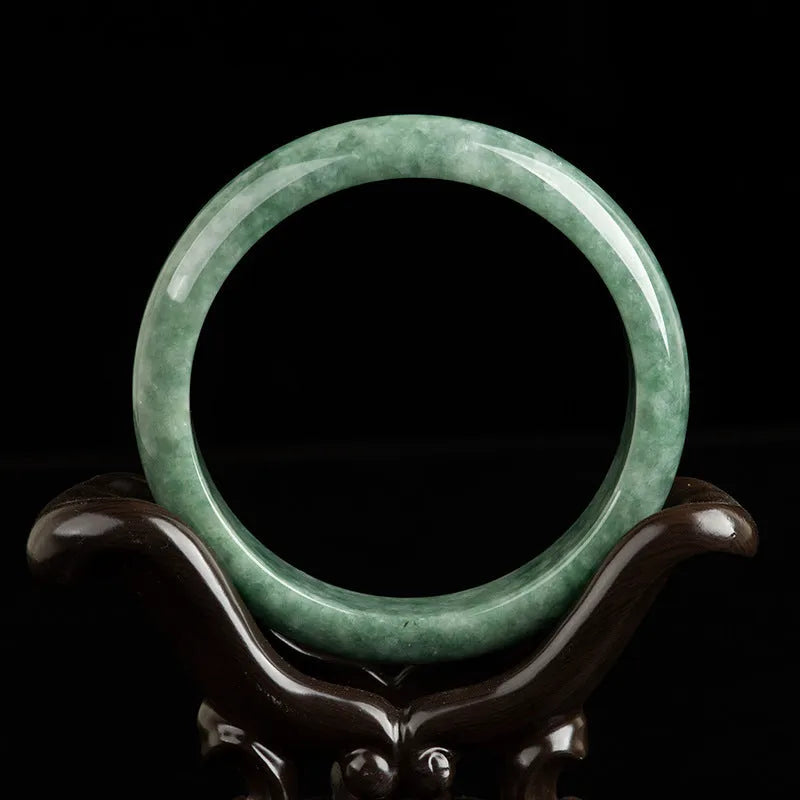 Dark pea green jade bracelet on a wrist, showing its simple band style and natural colour.