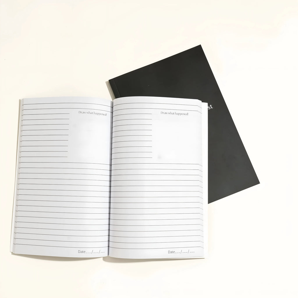 Black cover dream journal notebook with ruled pages open on a desk.
