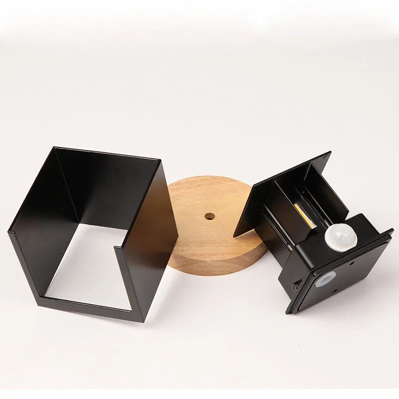 Small square aluminium wall lamp in black, mounted on a corridor wall, emitting a warm white light.