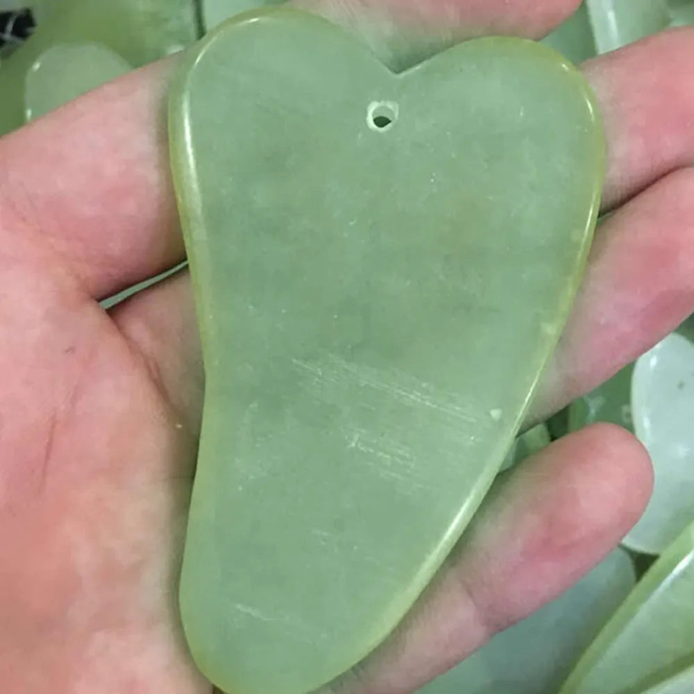 Natural green jade face massager roller and scraper set on a clean surface
