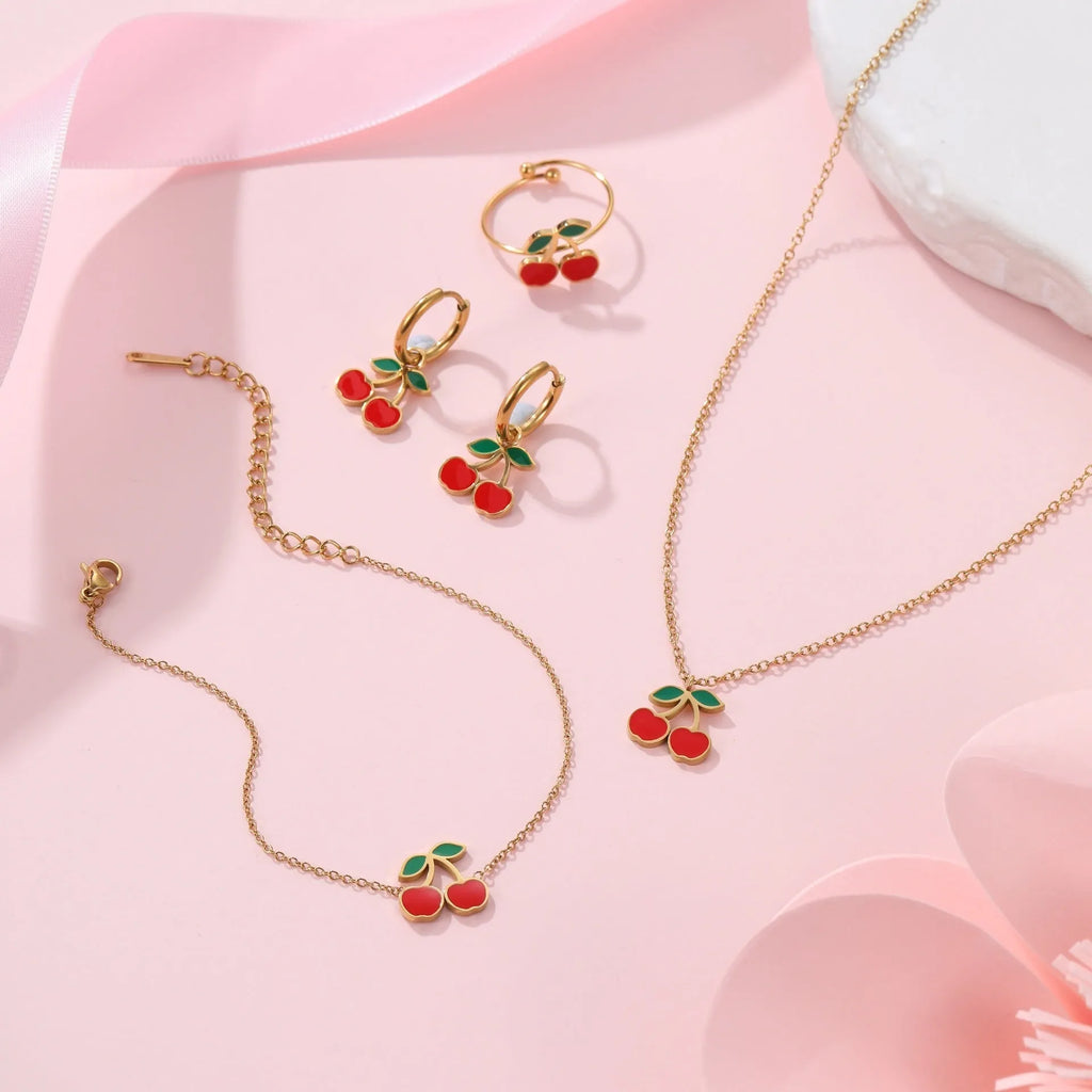 Complete cherry jewellery set showing stainless steel necklace, bracelet, earrings, and ring pieces with electroplated colour finishes