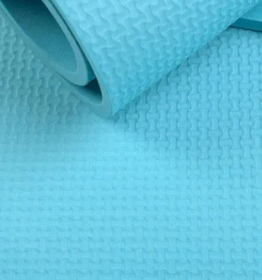 EVA foam yoga mat in blue, showing textured anti-slip surface, with a black OPP storage bag beside it.