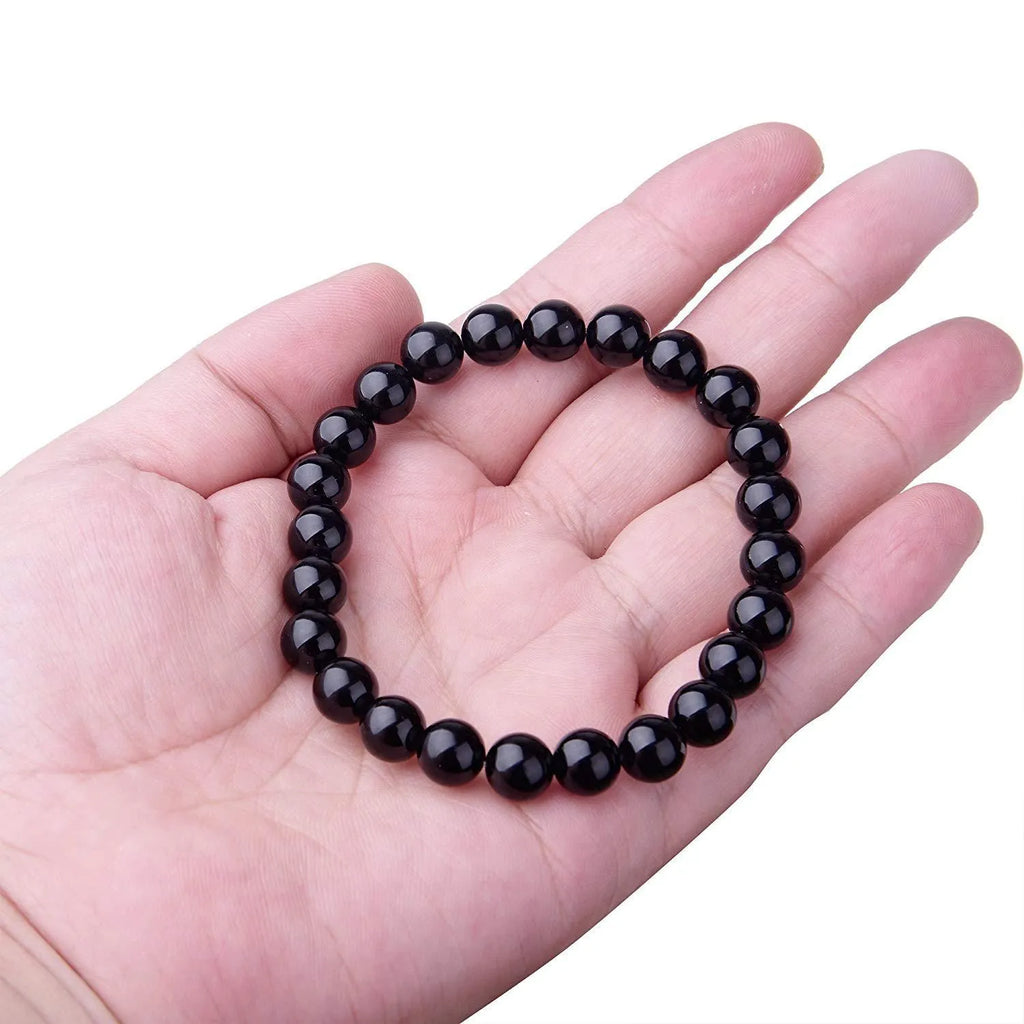 Close-up of a women's black onyx agate bracelet with 8mm geometric beads on a black elastic cord.