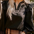 Black women's V-neck blouse with contrast stitching and ruffled long sleeves.