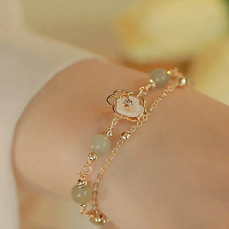 Yellow gold electroplated women's bracelet with butterfly and shell flower charms on a chain.