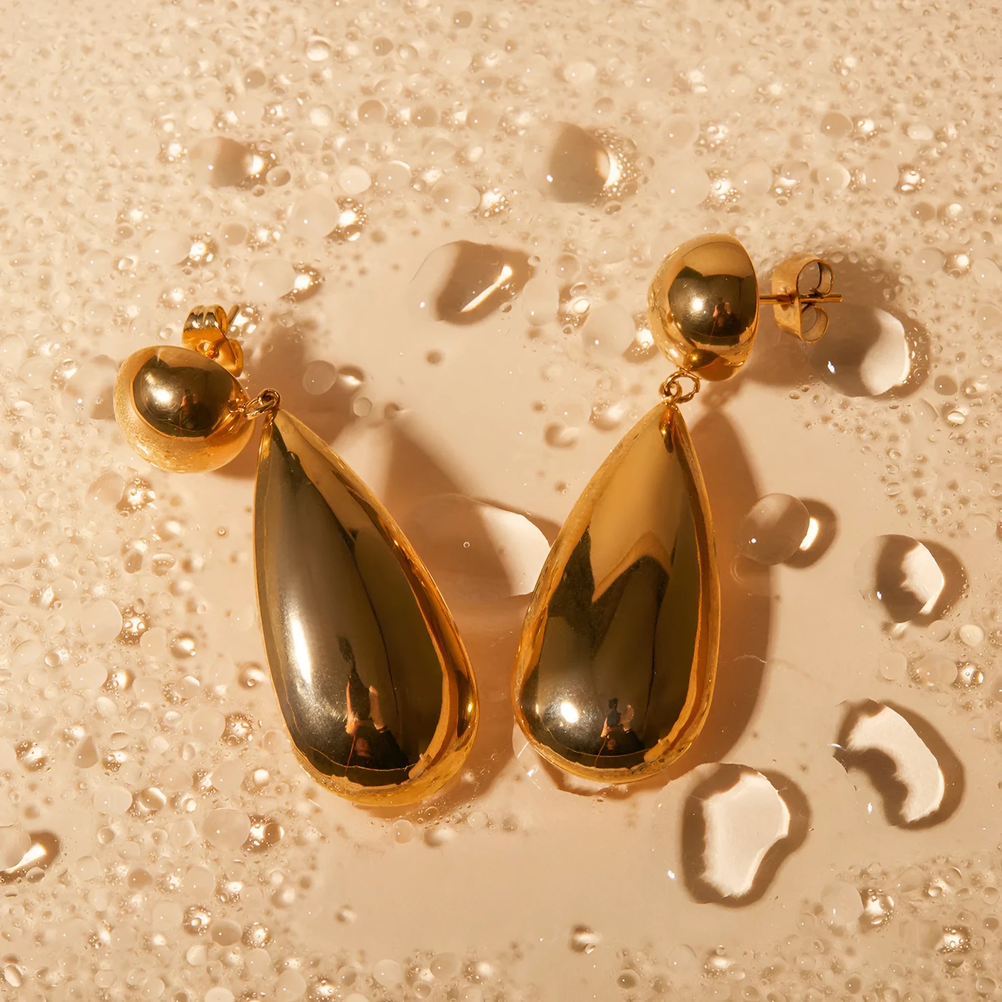 A pair of gold-coloured stainless steel earrings featuring geometric hemisphere shapes forming a water droplet design.