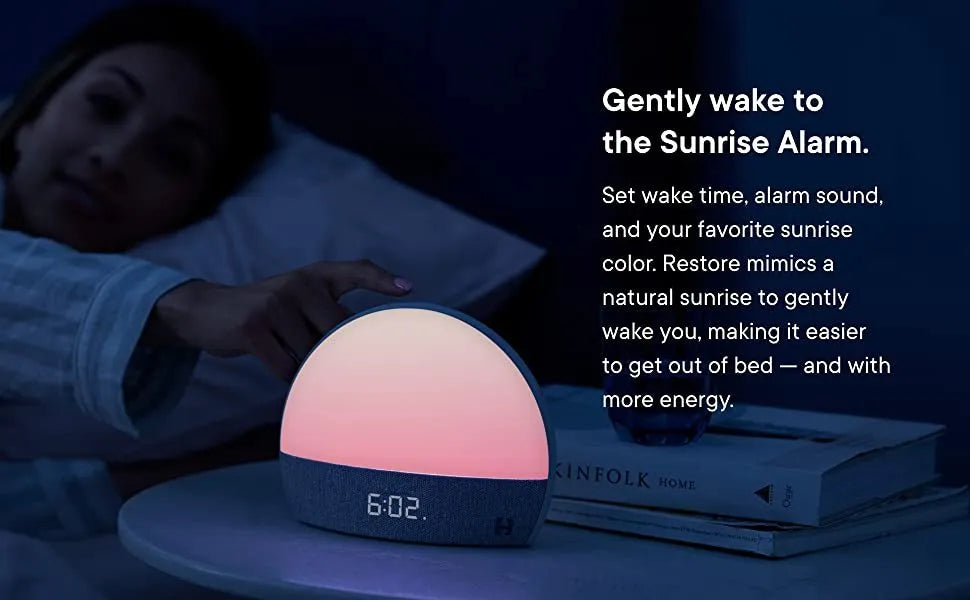Hatch Restore smart clock in light grey with a night light and white noise machine on a bedside table