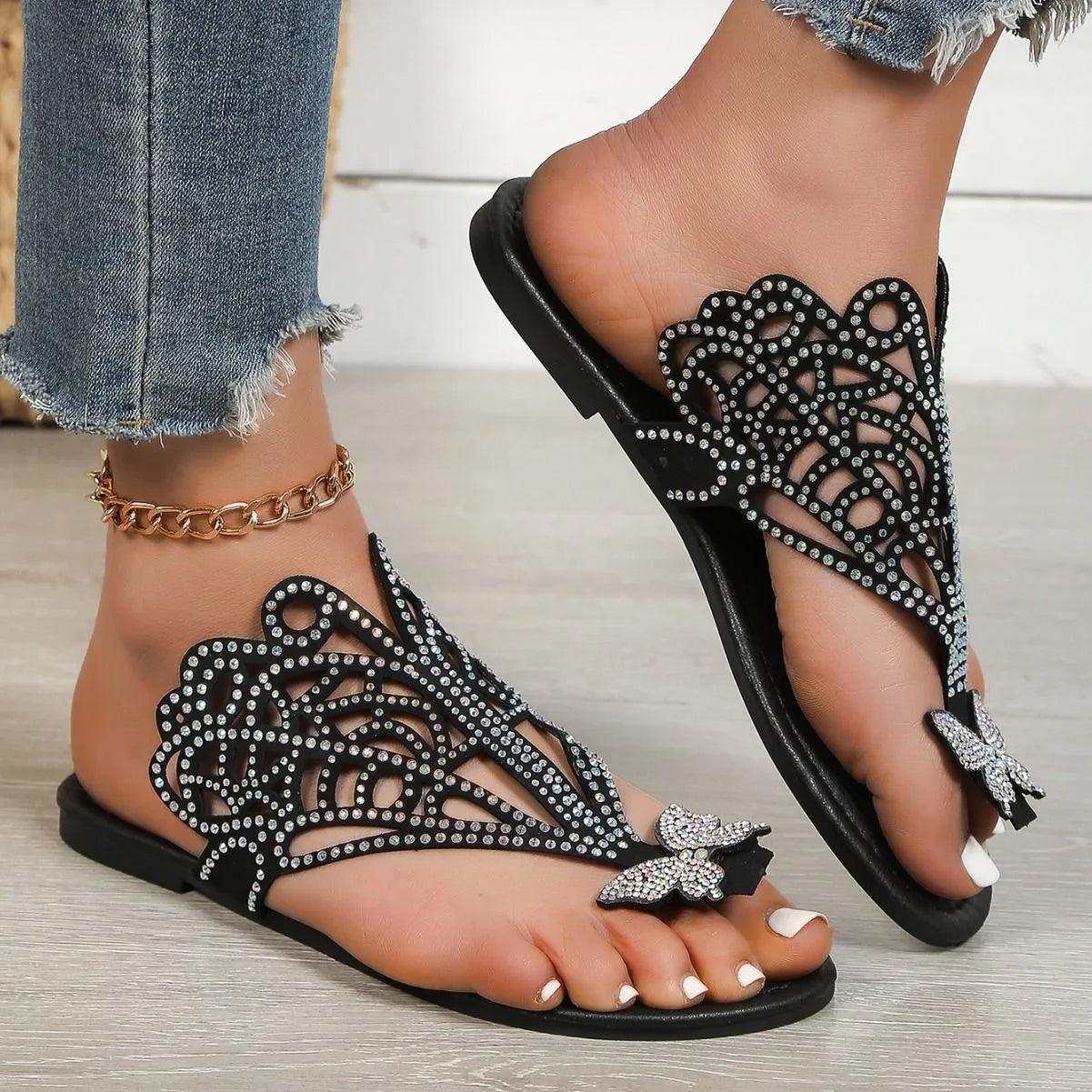Women's black slip-on sandals with rhinestone decoration on the flip-toe, showing the flat heel and rubber sole.