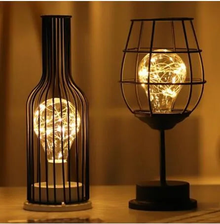Hollow wrought iron wine bottle shaped table lamp with warm white LED light on a wooden desk