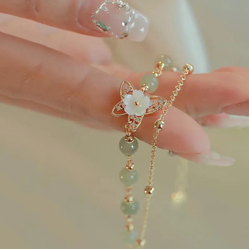 Yellow gold electroplated women's bracelet with butterfly and shell flower charms on a chain.