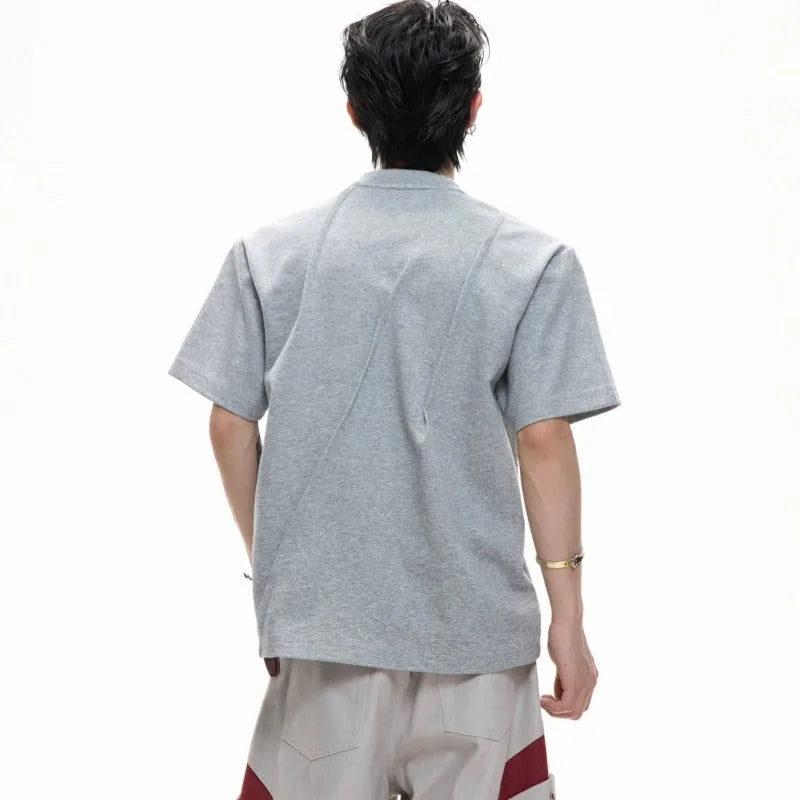 Man wearing a loose grey cotton T-shirt with three-dimensional pleated detailing on the front.