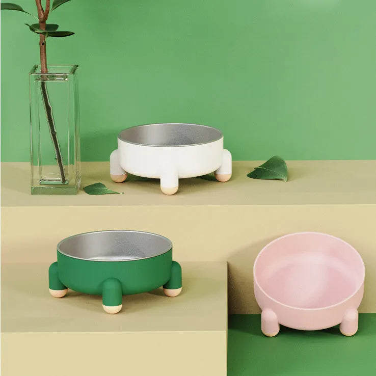 Green stainless steel pet bowl with a non-slip rubber ring and raised foot design on a wooden floor.