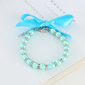 Small dog wearing a blue adjustable pearl and rhinestone necklace collar with a ribbon bow.