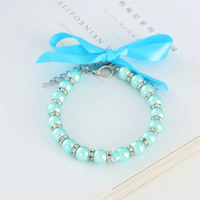 Small dog wearing a blue adjustable pearl and rhinestone necklace collar with a ribbon bow.