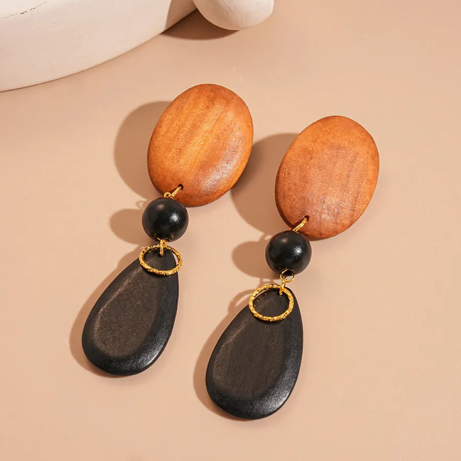 A pair of handmade brown and black wooden elliptical earrings in a retro style.