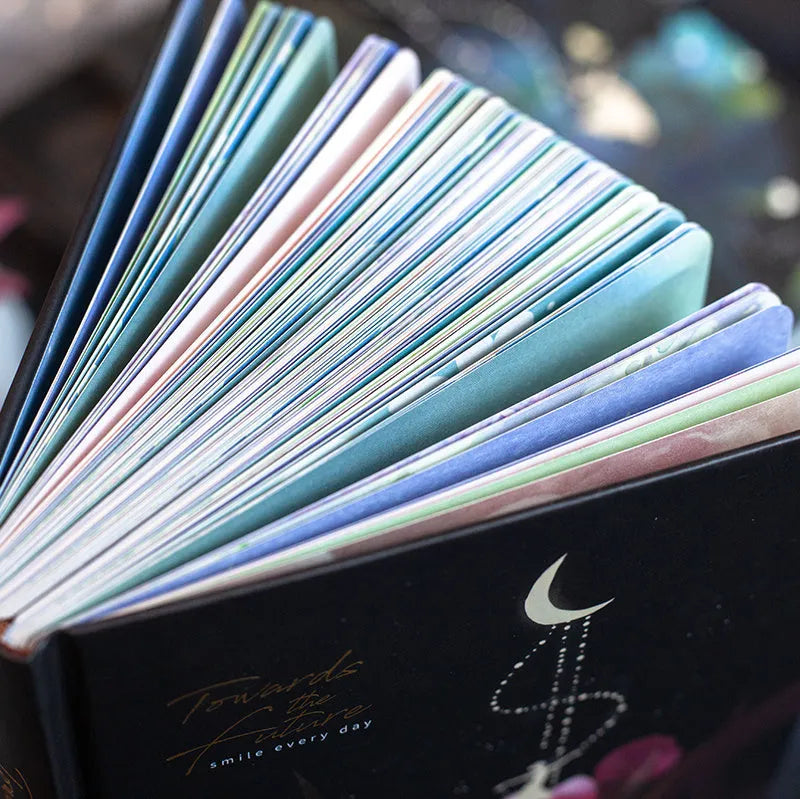 A5 notebook with luminous reflective cover shown in four colours: deep blue, gold, light blue, purple, open to reveal pages with colour illustrations.