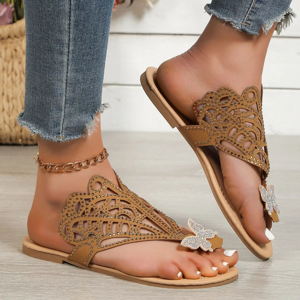Women's black slip-on sandals with rhinestone decoration on the flip-toe, showing the flat heel and rubber sole.