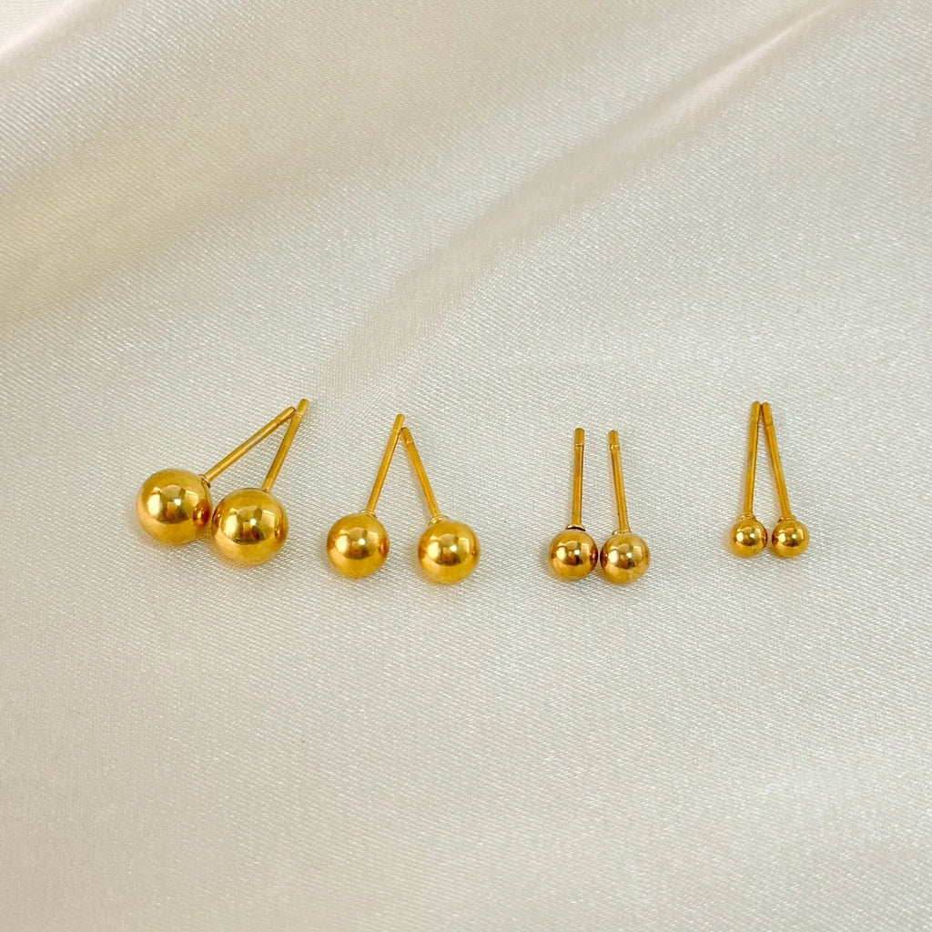 Minimalist round ball stud earrings in gold and silver tones on a plain background.