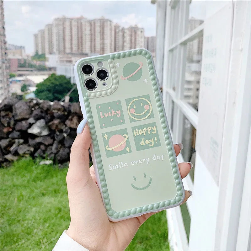 Green flexible TPU iPhone case with a geometric smiley face and polka dot frame design on the back.