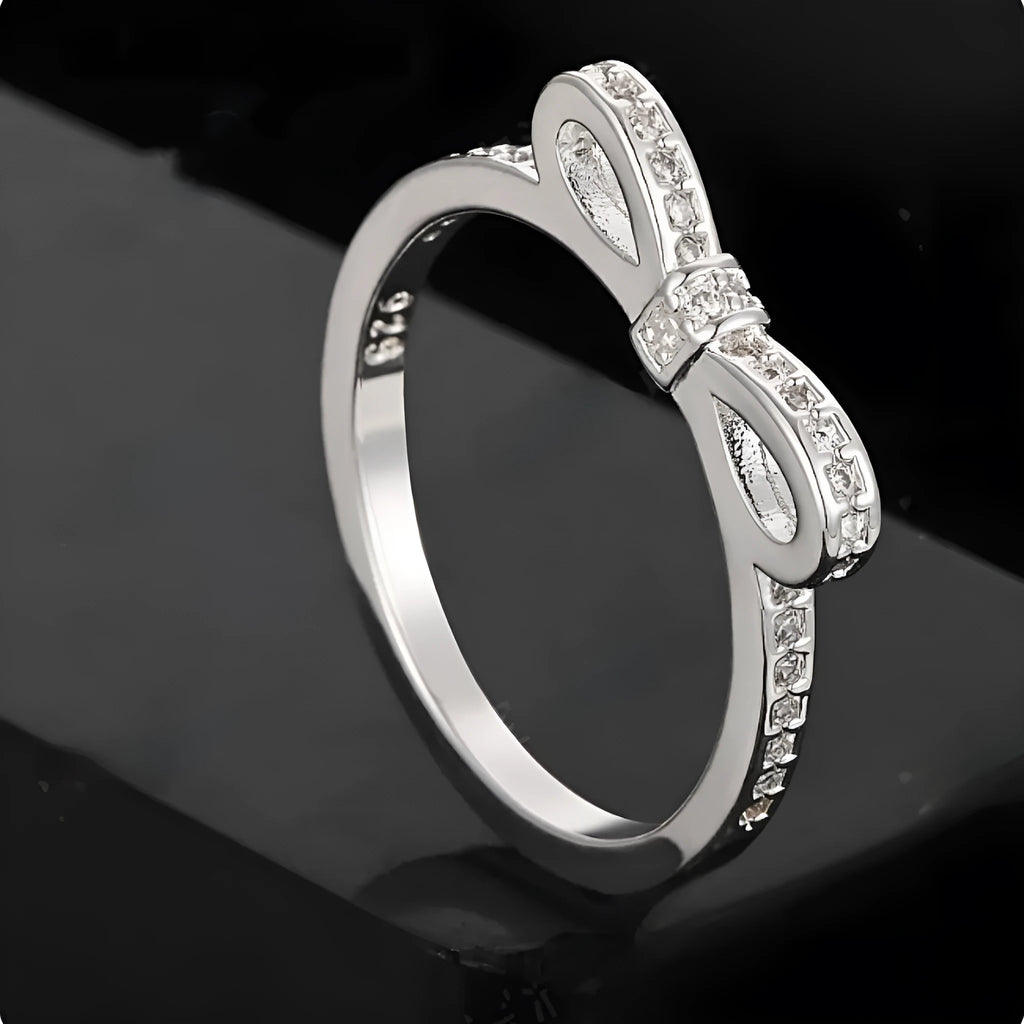 Silver couple ring with bow shape and rhinestone zircon crystals on finger.