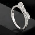Silver couple ring with bow shape and rhinestone zircon crystals on finger.