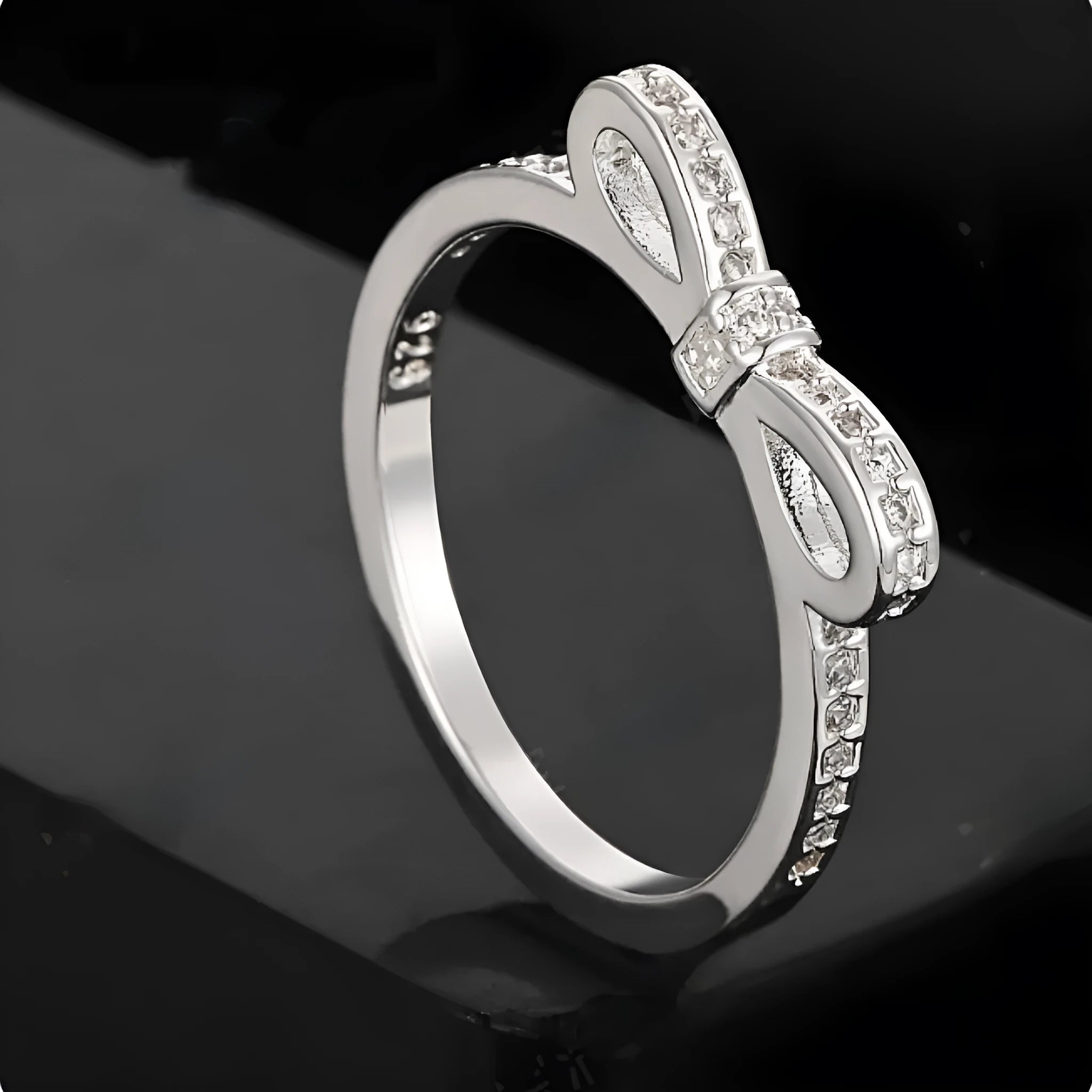 Silver couple ring with bow shape and rhinestone zircon crystals on finger.