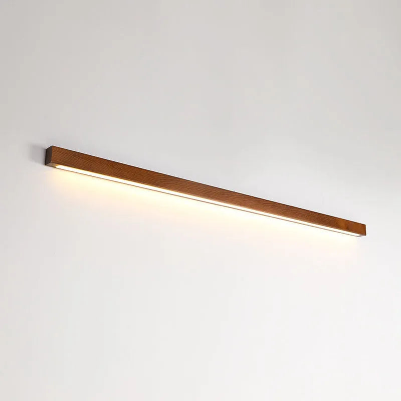 Walnut colour wood and acrylic strip wall lamp in three lengths on a white wall.