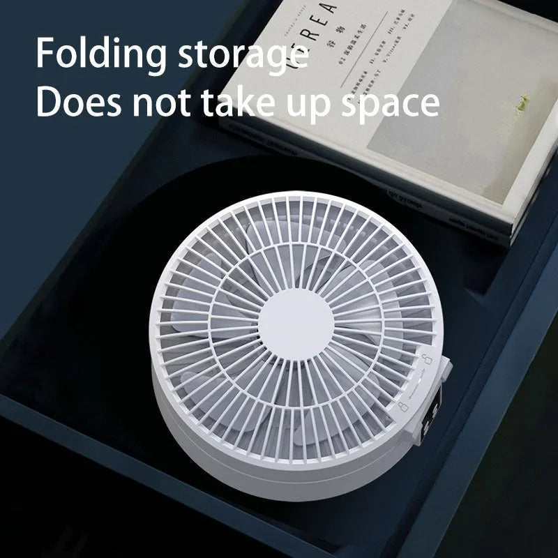 White portable USB folding desk fan with remote control and warm night light on a table.