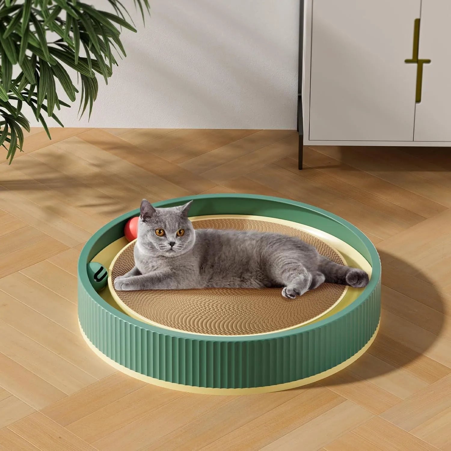Large green cardboard cat scratching board with three coloured ball toys attached on a flat surface.