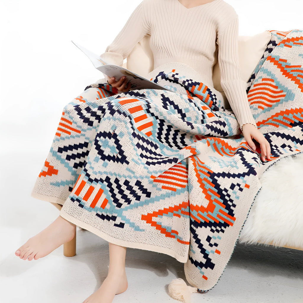 Bohemian-style acrylic sofa blanket with tassel trim shown in a beige and orange colour.