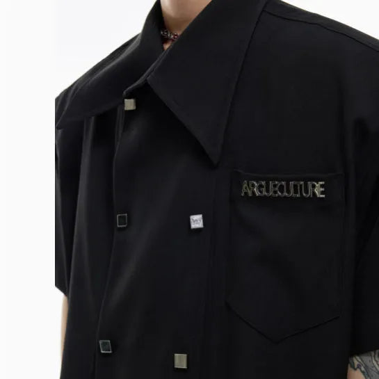 A man wearing a loose-fit black short-sleeved casual shirt with a lapel collar and decorative splicing detail.
