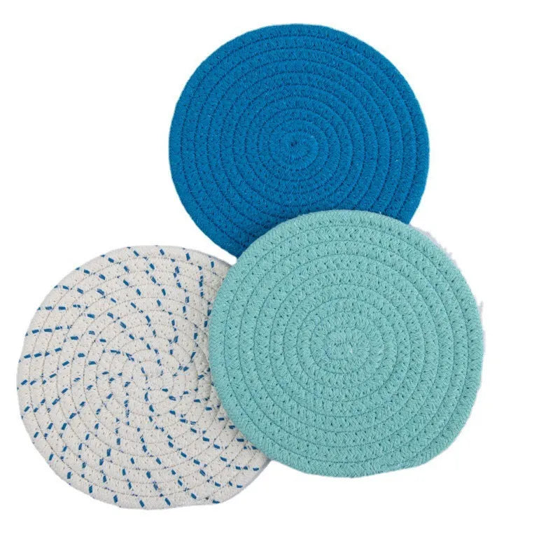 Three round blue cotton cord coaster placemats on a wooden table.